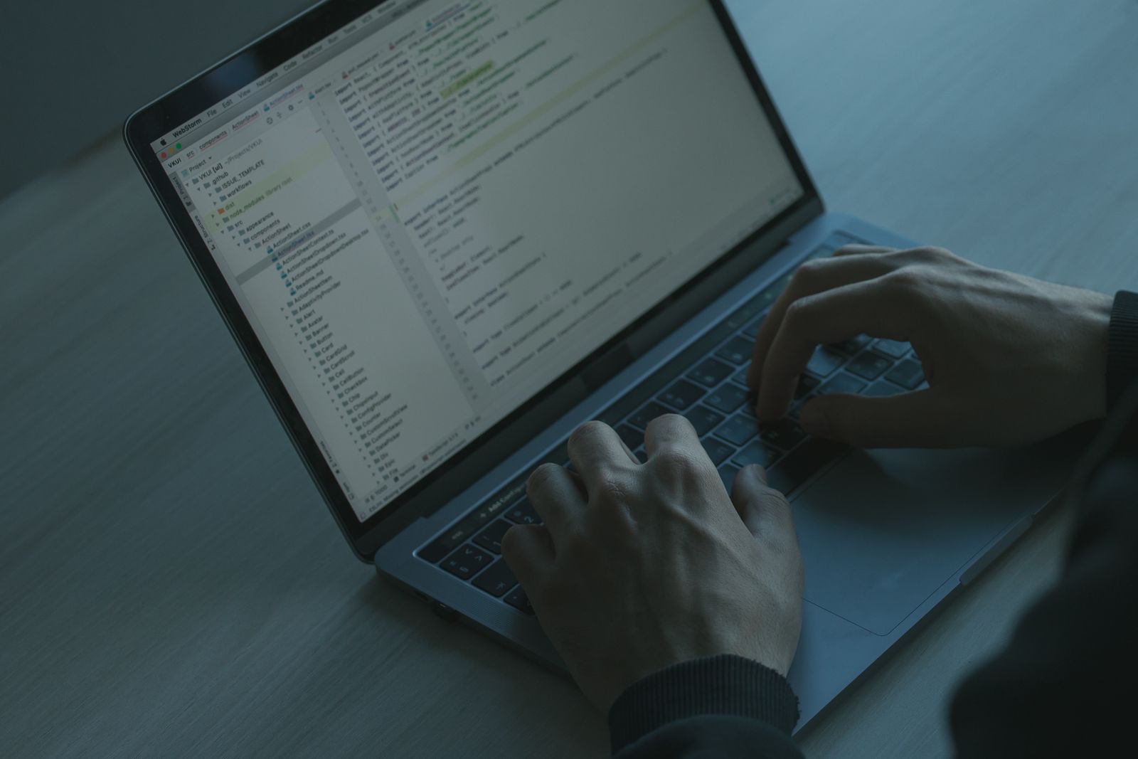 Hands typing on a laptop in a darkened room